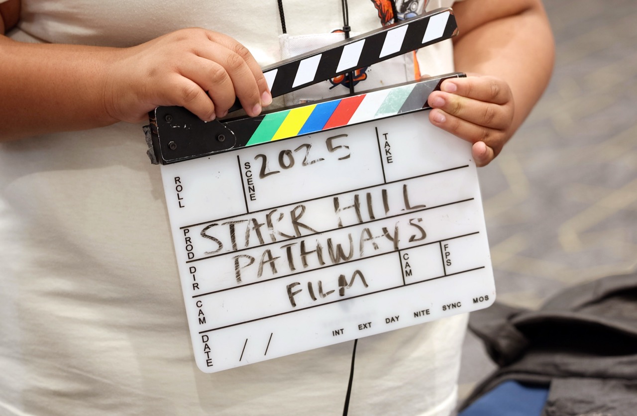 A student holding a slate that reads "2025 Starr Hill Pathways Film"