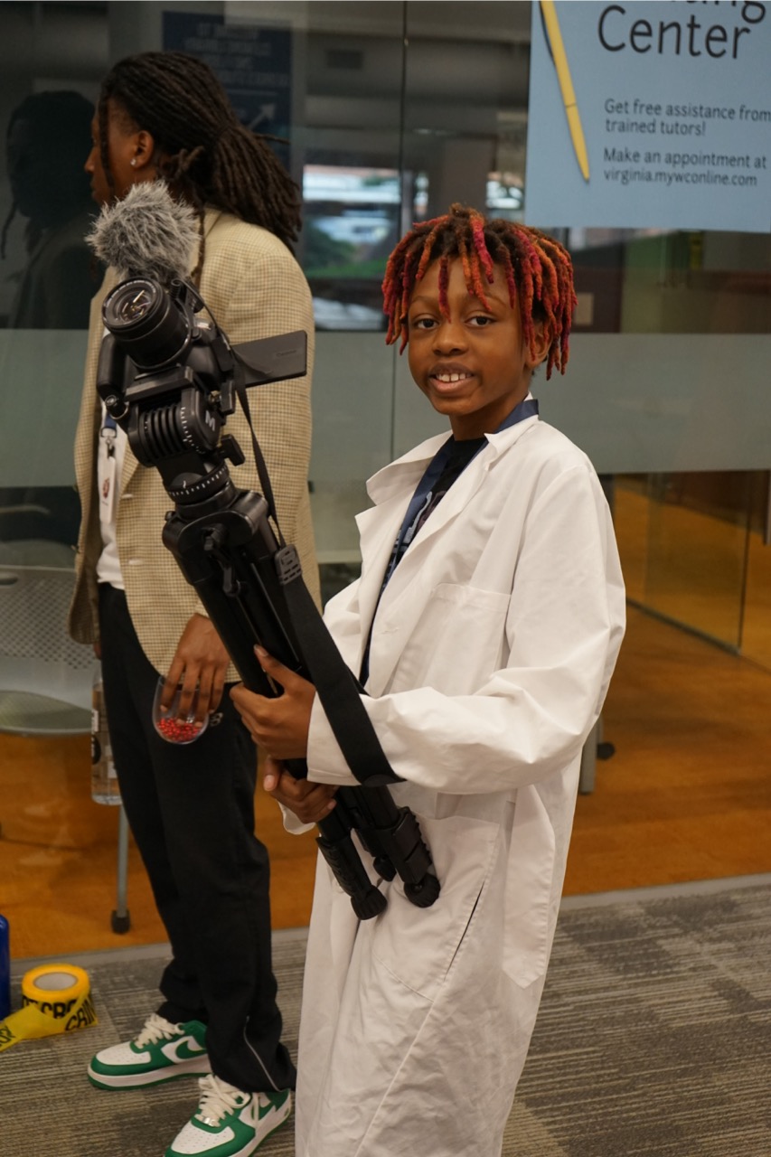 A child holding a camera while wearing a lab coat